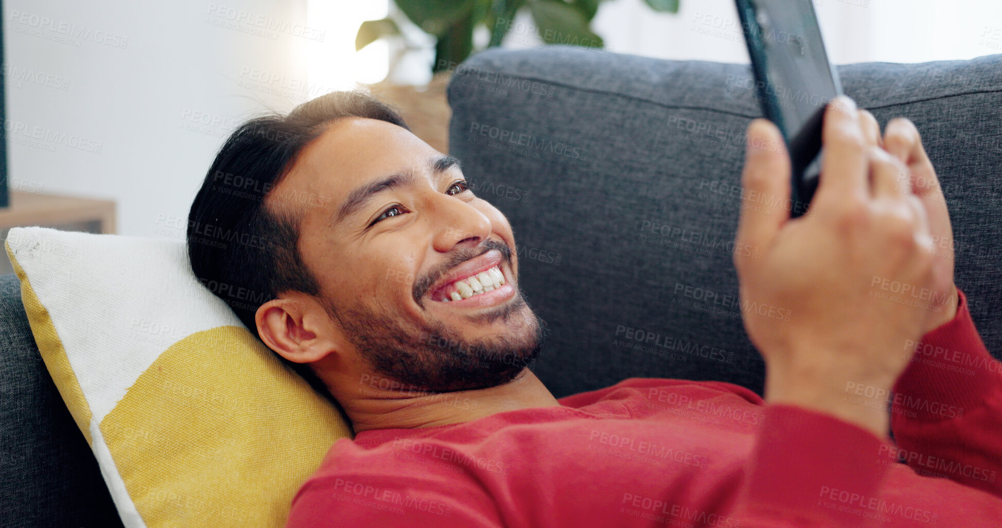 Buy stock photo Phone, smile and Asian man on sofa with social media, comic or laugh at funny text while streaming at home. Happy, smartphone and Japanese male in a living room with app, meme or gif communication