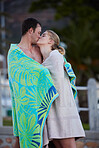 Sea, kiss and young couple in beach towels with love and bonding after engagement outdoor. Vacation travel, trust and happiness of a woman and man together by a ocean in nature sharing a sweet moment