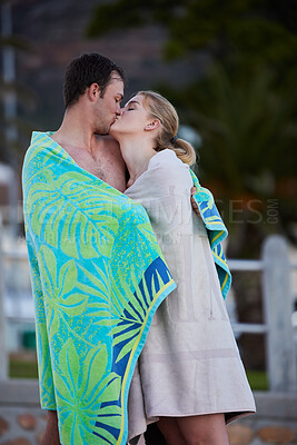 Buy stock photo Sea, kiss and young couple in beach towels with love and bonding after engagement outdoor. Vacation travel, trust and happiness of a woman and man together by a ocean in nature sharing a sweet moment