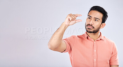 Buy stock photo Hand gesture, size and mockup with a man in studio on a gray background to measure product placement space. Tiny, small and scale with a handsome young male sizing or measuring mock up on a wall