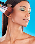 Makeup, brushes and Indian woman with foundation, facial treatment and girl against a blue studio background. Female, lady and tools for cosmetics, skincare and beauty for confidence and self care