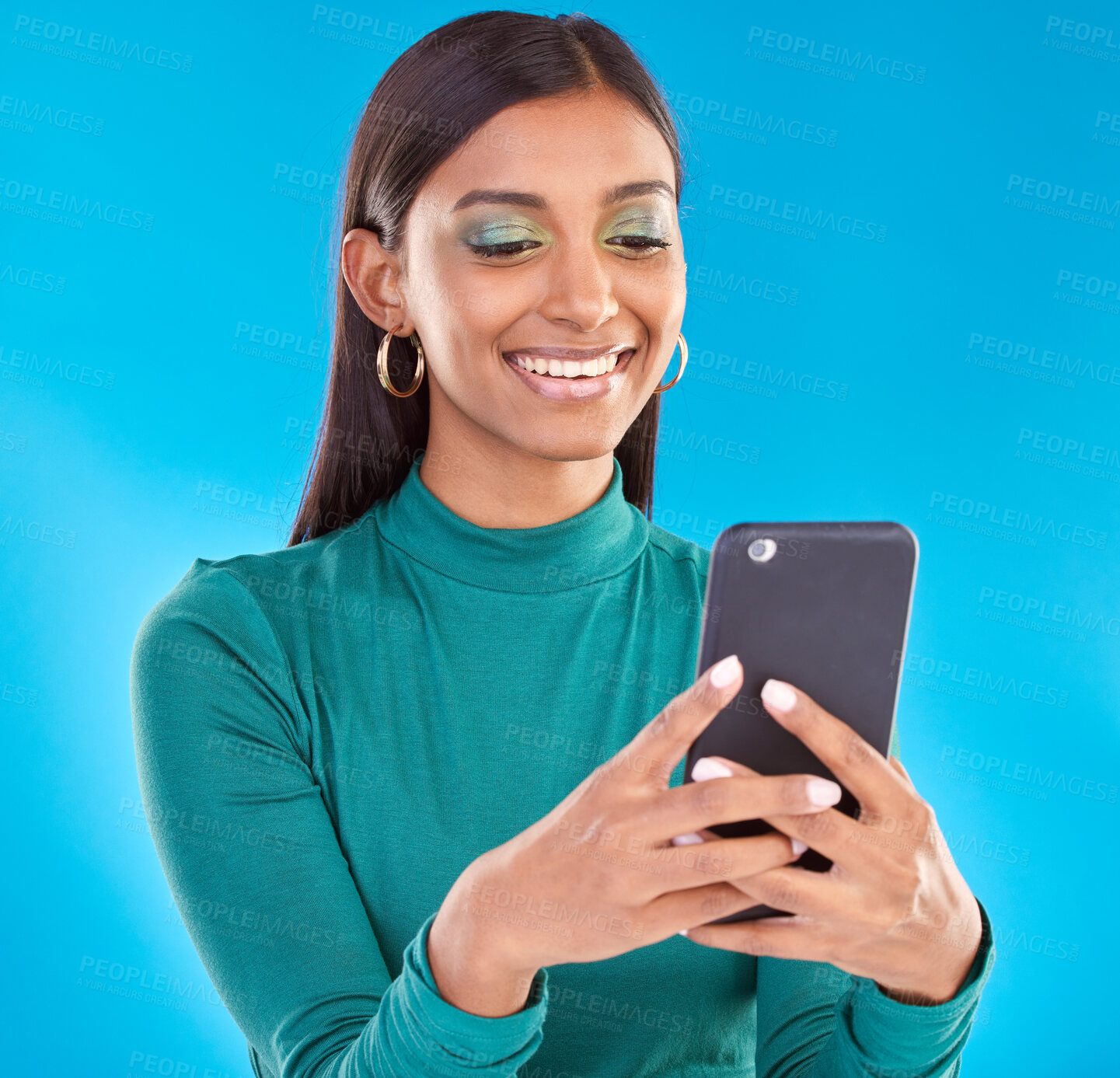 Buy stock photo Happy woman, smile and typing on phone in studio for communication, social media or mobile app. Gen z model person with smartphone in hands on a blue background for network connection or internet