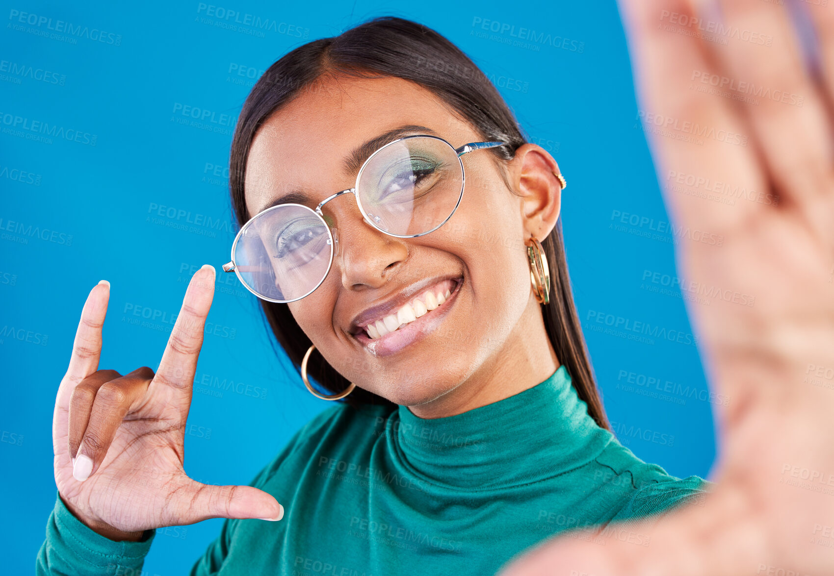 Buy stock photo Woman, fashion and selfie portrait with rock on hand for gen z attitude on blue background with glasses. Face of happy model person in studio with smile or cool sign emoji for beauty and motivation