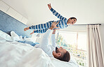 Father, son and dad playing with his child on a bed holding him having fun in a bedroom feeling happy, carefree and excited. Parent, kid and dad bonding with young boy in a house together 