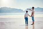 Hand holding, happy and father with son at beach and pointing for summer break, vacation and travel. Bonding, affectionate and holiday trip with man and boy for relax, care and free time on weekend