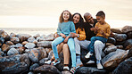 Adventure, beach and family relaxing on rocks while on summer vacation, travel or weekend trip. Happy, smile and portrait of mother bonding with her children and husband by the ocean while on holiday