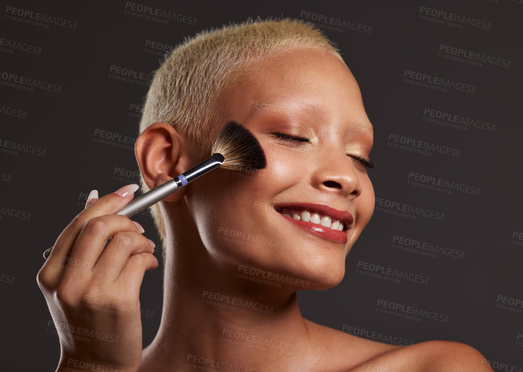 Buy stock photo Woman, smile and makeup brush for beauty cosmetics, skincare or facial treatment against a gray studio background. Happy beautiful female model applying cosmetic product on face for self care or love