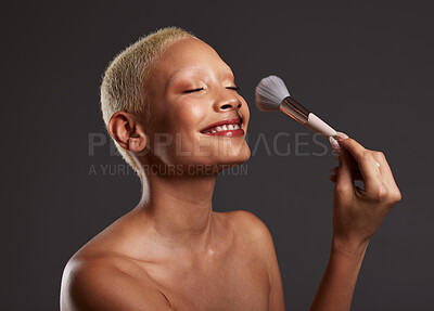 Buy stock photo Woman, smile and makeup brush for facial beauty cosmetics, skincare or treatment against a gray studio background. Happy beautiful female model applying cosmetic product on face for self care or love