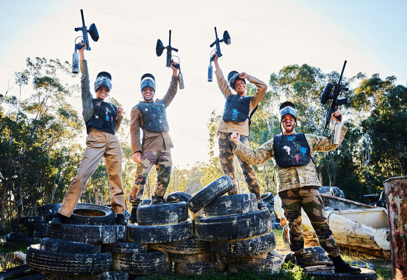 Buy stock photo Team, paintball and portrait in celebration for winning, victory or achievement standing on tires together in nature. Group of people enjoying win, success or teamwork with guns in the air for sports