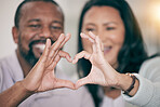 Hands, love and heart with a couple in their home to relax together in the living room closeup. Hand gesture, emoji or romance with a senior man and woman bonding while sitting in their house