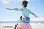 Beach, blue sky and black man with child on back on playful family holiday in Australia with freedom and energy. Travel, fun and happy father and girl playing, flying and bonding together on vacation