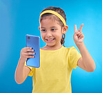 Phone, girl kid and peace sign selfie in studio isolated on a blue background. Technology, v hand emoji and smile of child with mobile smartphone to take pictures for happy memory or social media.
