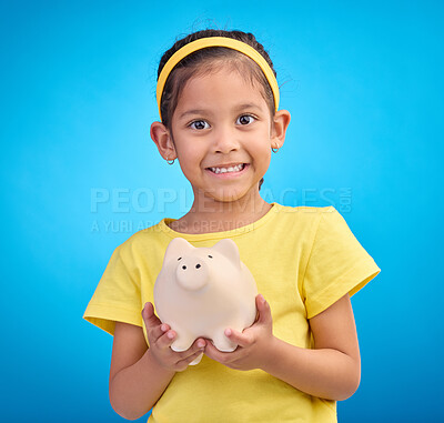 Buy stock photo Face portrait, piggy bank and girl child in studio isolated on a blue background. Happy, smile and kid with cash box, savings or financial, investment or learning budget, finance growth or money.