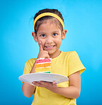 Birthday cake, portrait and young girl with sweet in studio eating icing for party event dessert. Celebration, rainbow food and hungry kid in a isolated and blue background youth ready to celebrate