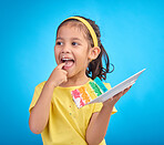 Happy, tasting and girl with cake, excited and cheerful against blue studio background. Young person, Latino female child and kid with dessert, happiness or cheerful with licking finger and celebrate