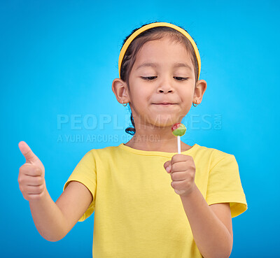 Buy stock photo Candy, happy and child with lollipop and thumbs up on blue background with happiness, smile and excited. Party, childhood and young girl with hand sign eating sweets snack, sugar and treats in studio
