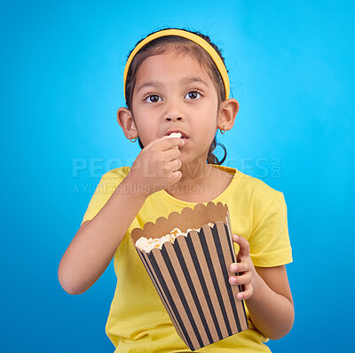 Buy stock photo Popcorn, eating and focus with girl in studio for food, cinema and relax. Television, movie and film with child and snack for streaming service, subscription and tv isolated on blue background