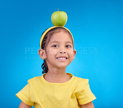Buy stock photo Portrait, smile and girl with apple on head on blue background for nutrition, healthy eating and diet. Food, youth and face of happy young girl in studio with fruit for organic, vitamins and wellness