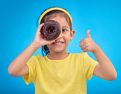 Buy stock photo Donut, eye and thumbs up with portrait of girl in studio for junk food, sugar and happiness. Snack, cake and cute with face of child and dessert for eating, positive and chocolate on blue background
