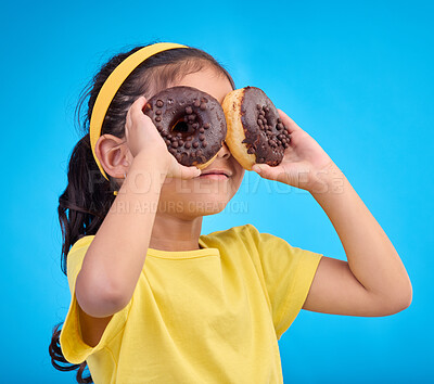 Buy stock photo Doughnuts, eyes and face of playful child with food isolated against a studio blue background with a smile. Adorable, happy and cute young girl or kid excited for sweet sugar donut calories