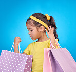 Girl, shopping and gift bags from birthday party, event or celebration with a present in a studio. Shop choice, bag and little child looking at presents with isolated and blue background with a kid
