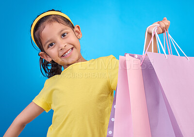 Buy stock photo Girl portrait, shopping and gift bags from birthday party, event or celebration with a present in studio. Shop, bag and happy child looking at presents with isolated and blue background with a kid