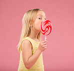 Candy, sweets and lollipop with girl in studio for sugar, party and carnival food isolated on pink background. Cute, positive and youth with child and eating colorful snack for playful and treats  