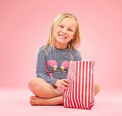 Buy stock photo Popcorn, food and happy girl portrait in a studio with pink background sitting with movie snacks. Snack, happiness and hungry child with a paper bag and chips eating and feeling relax with a smile