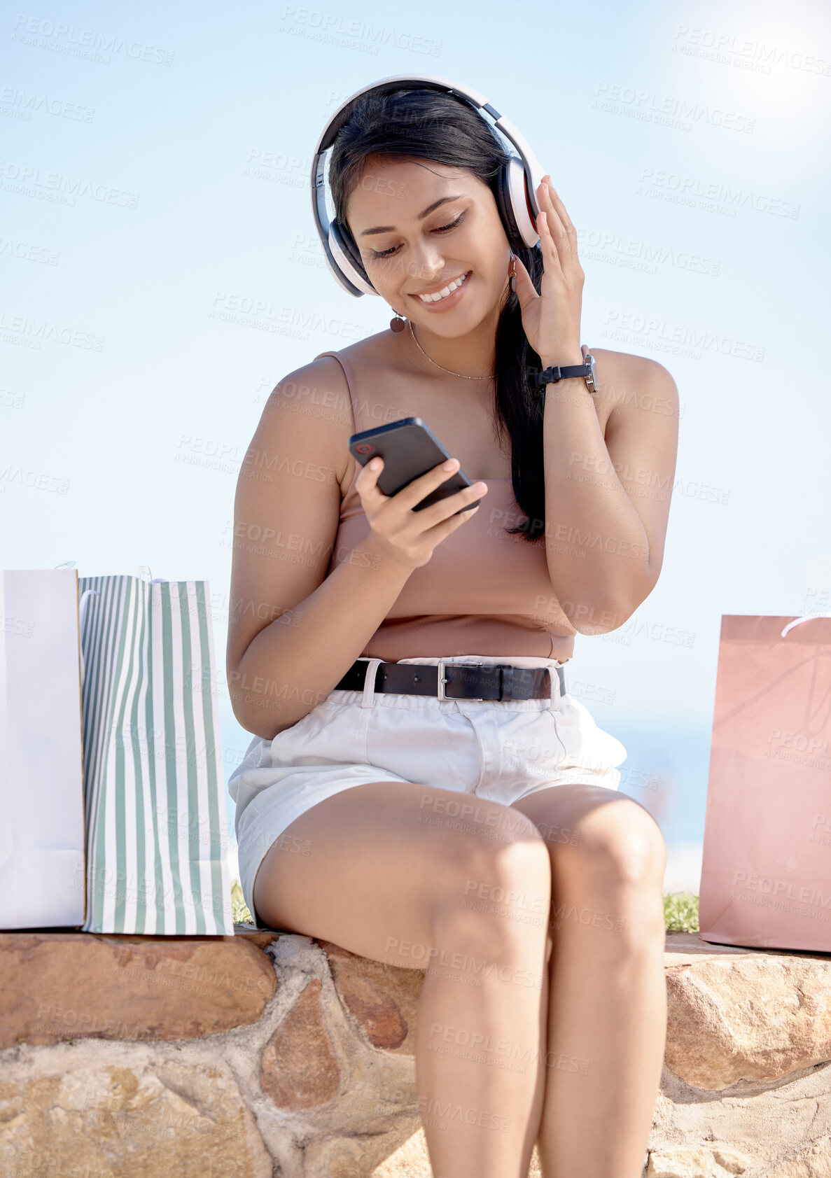 Buy stock photo Woman relax after shopping, phone and headphones, listening to music outdoor with retail therapy and rest. Happy female, paper bag and communication with chat on social media app and technology