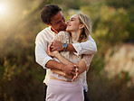 Couple, love and kiss outdoor at sunset for love, care and romance with hands on face on a date. Young man and woman together on valentines day with lens flare, peace and freedom in nature forest