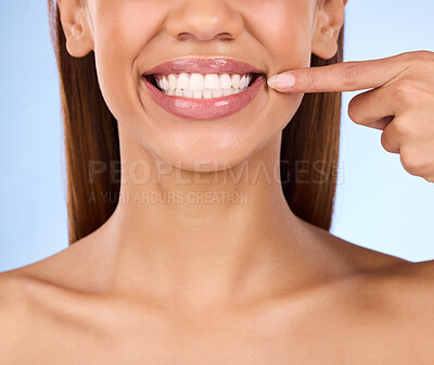 Buy stock photo Dental, pointing and teeth with smile of woman in studio for beauty, clean and self care. Oral hygiene, natural and cosmetic treatment with girl model on blue background for veneers, fresh or results