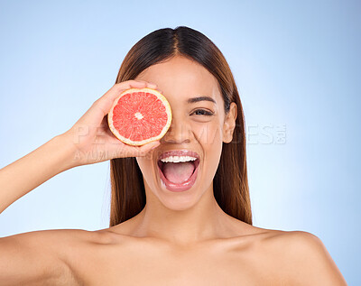Beauty, excited woman and grapefruit portrait for skincare dermatology cosmetic. Female model on blue background for self care, facial glow and healthy fruit for natural skin and happy face in studio