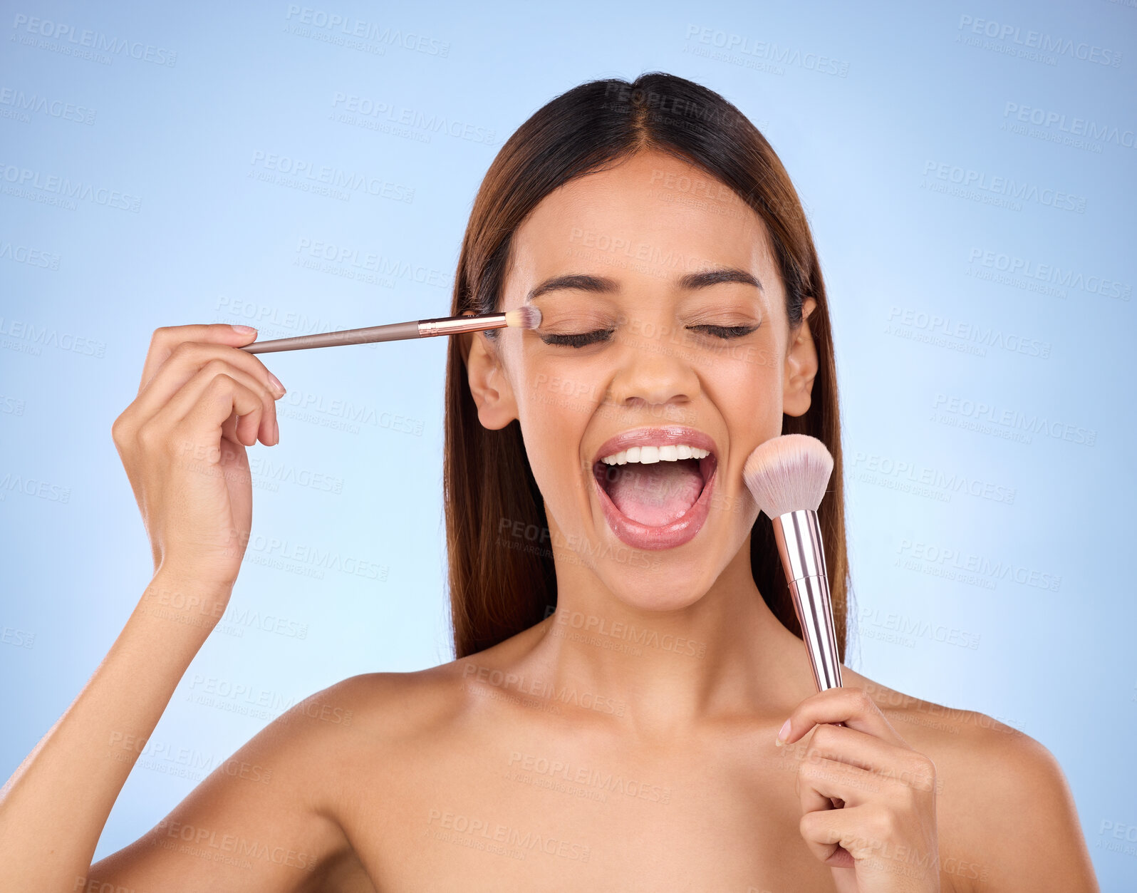 Buy stock photo Beauty, woman and brush for makeup on face with cosmetics in studio. Aesthetic female model person on a blue background excited for self care, facial glow and application for powder and shine on skin