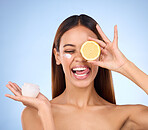 Woman, moisturizer cream and lemon for natural skincare, beauty and vitamin C against a blue studio background. Female holding citrus fruit, creme or lotion for healthy organic nutrition or facial