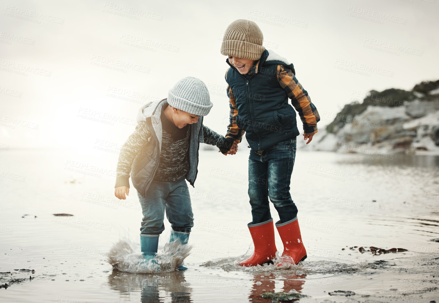 Buy stock photo Beach, boots and children in water together, holding hands and playing in waves with smile. Fun, holiday and brothers, happy boys on ocean vacation at sunset, jumping and splash on evening sea walk.