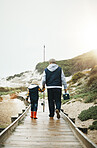 Fishing, child and grandfather walking on beach pier with tools from back, bonding time on winter weekend. Nature, family and old man with small boy holding hands and learning catch fish in Greece.
