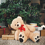 Christmas, gift and festive with a teddy bear by a tree, ready for celebration during the holiday season. December, event and a stuffed animal sitting in the living room of an apartment as a present