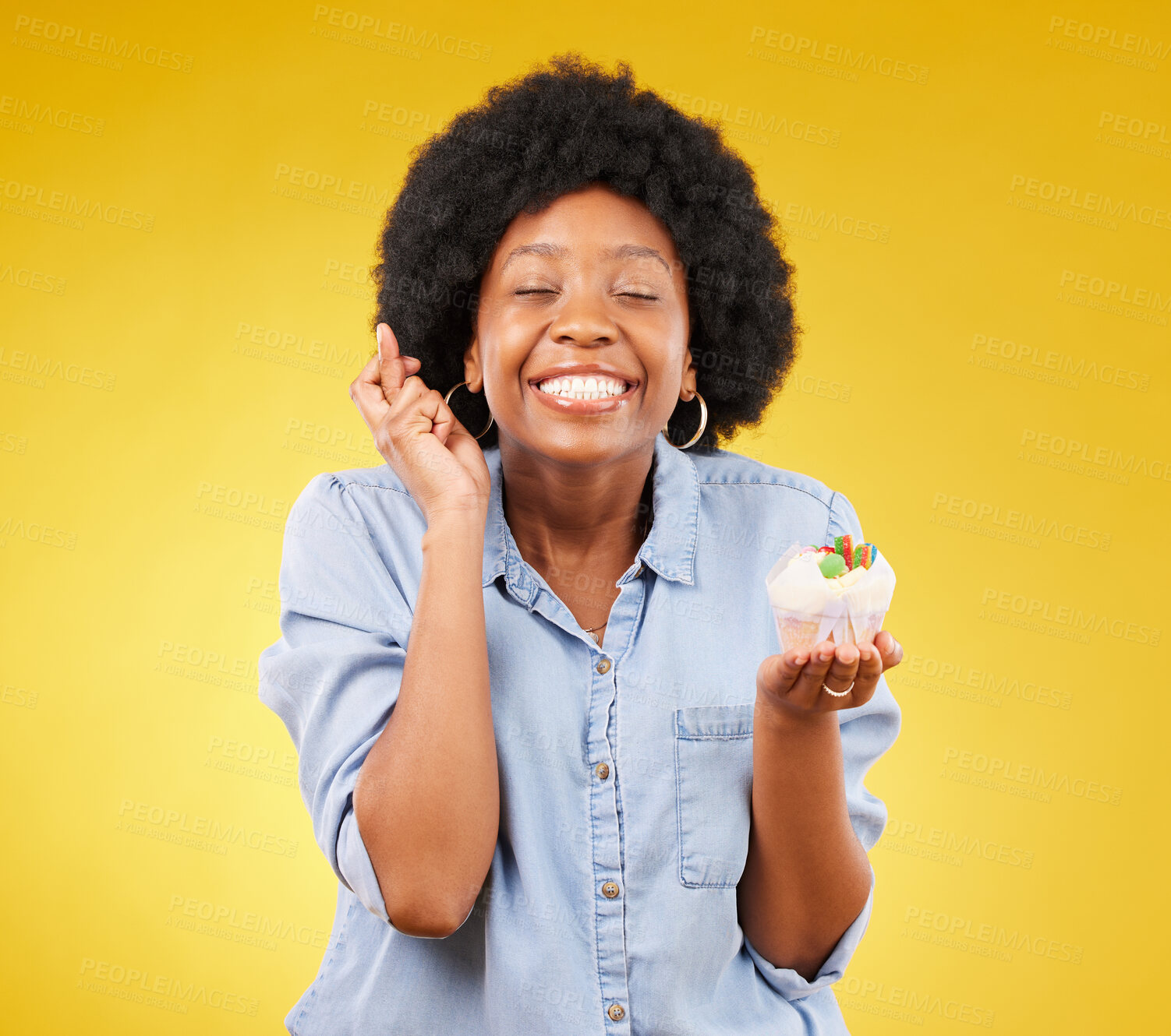 Buy stock photo Birthday, wish and cupcake with a black woman on a yellow background in studio for celebration. Happy, smile and dessert with an attractive young female celebrating a special event on a color wall