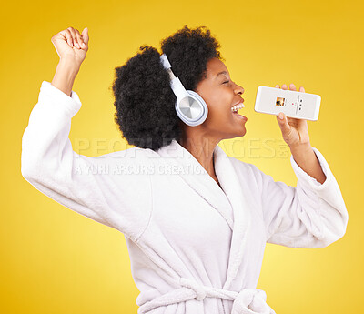 Buy stock photo Black woman, music headphones and singing with phone in studio isolated on a yellow background. Karaoke singer, bathrobe and happy female dance with mobile microphone while streaming podcast or radio