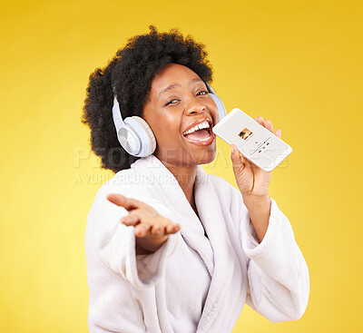 Buy stock photo Black woman, music headphones and singing with phone in studio isolated on a yellow background. Karaoke singer, bathrobe and face portrait of happy female with mobile while streaming podcast or radio