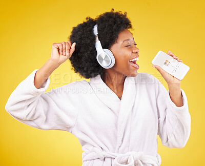 Buy stock photo Black woman, singing and happiness in a bathrobe with phone in studio isolated on a yellow background. Singer, headphones or happy female dance with mobile microphone while streaming podcast or radio
