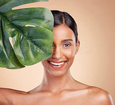 Portrait, beauty and palm leaf with a model woman in studio on a beige background for natural skincare. Face, plants and nature with an attractive young female posing for cosmetics or luxury wellness