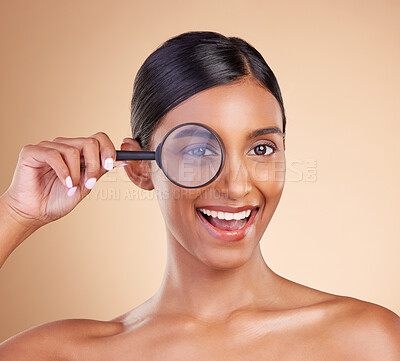 Buy stock photo Portrait, beauty and magnifying glass with a model woman in studio on a beige background searching for skincare. Face, eye and investigation with an excited young female looking for luxury cosmetics