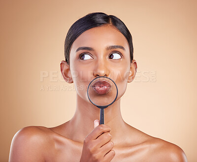 Buy stock photo Mouth, lips or woman with magnifying glass in studio on beige background searching for facial beauty. Face, headshot or young Indian girl looking for luxury self care cosmetics, lipstick or makeup
