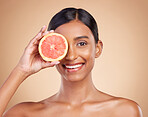 Portrait, beauty and grapefruit with a model woman in studio on a beige background to promote skincare. Face, eye and fruit with an attractive young female posing for natural or organic cosmetics