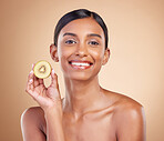 Portrait, skincare and kiwi with a model woman in studio on a beige background to promote beauty. Face, fruit and natural with an attractive young female posing for organic or luxury cosmetics