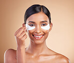 Eye patch, beauty and portrait of a woman in studio for skincare, dermatology and cosmetics. Happy Indian female model with smile and collagen gel mask for self care facial on brown background