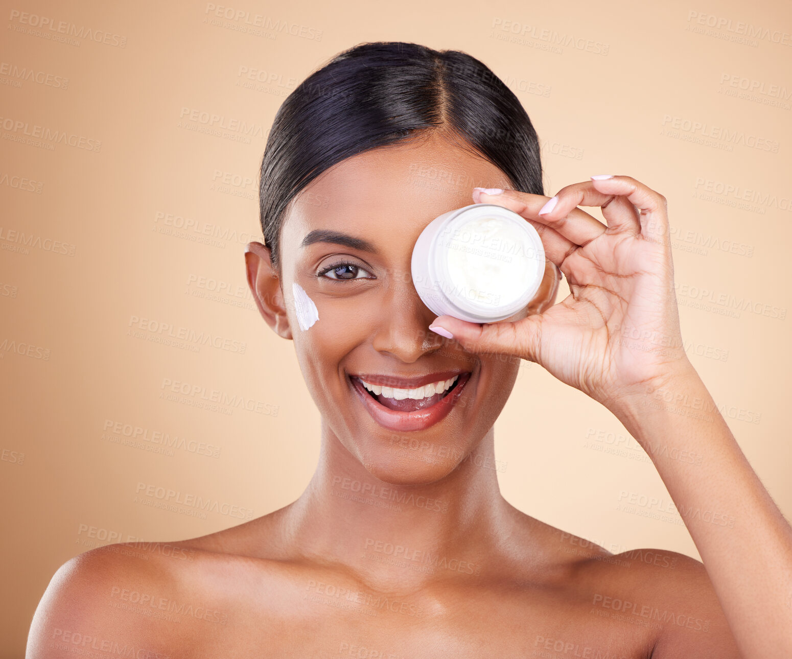 Buy stock photo Beauty, face cream and portrait of a woman in studio for skincare, dermatology and cosmetics. Happy Indian female model with smile and lotion on hand for self care moisture facial on brown background