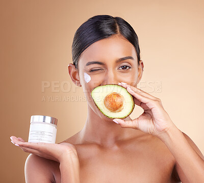 Buy stock photo Beauty, avocado and face cream woman portrait in studio for cosmetics, skin glow and natural product. Indian female model wink on beige background for skincare, facial self care and organic container