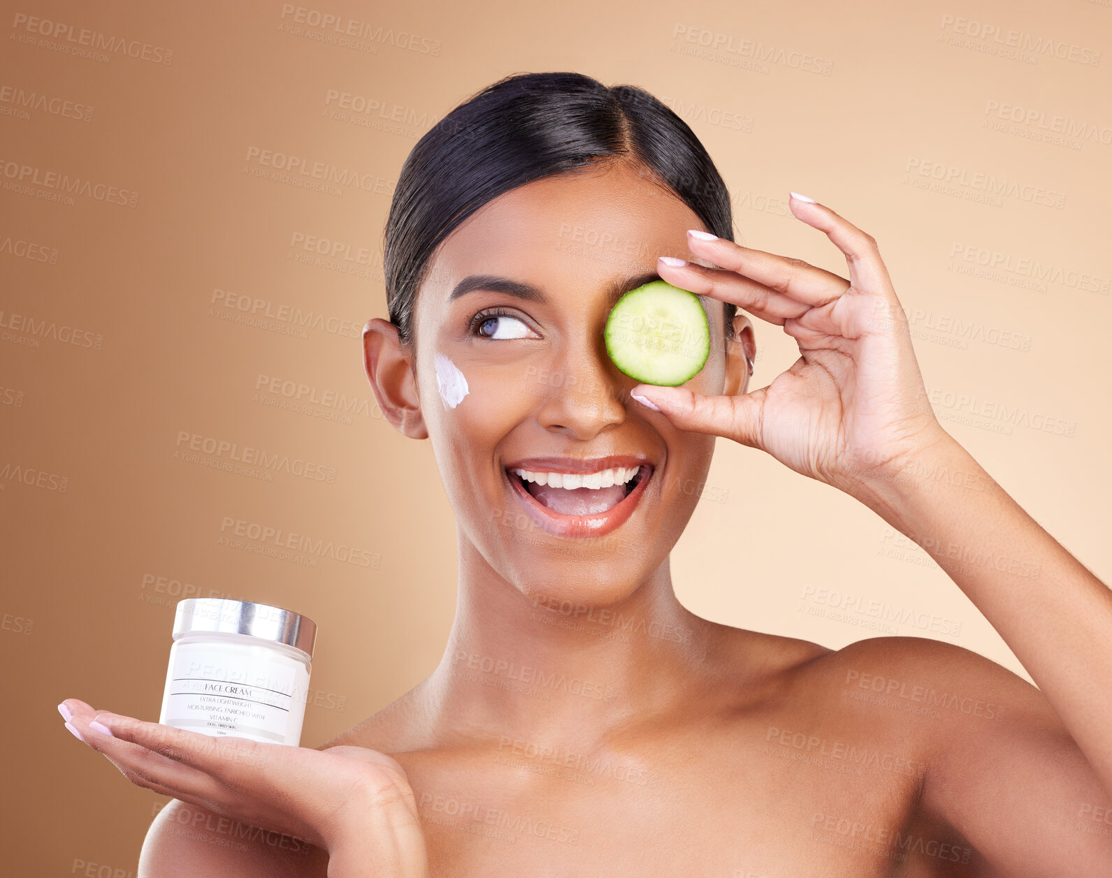 Buy stock photo Beauty, skincare and Indian woman with cucumber, cream and dermatology against a brown studio background. Female, cosmetics and happy lady with natural care, lotion and healthy detox with grooming